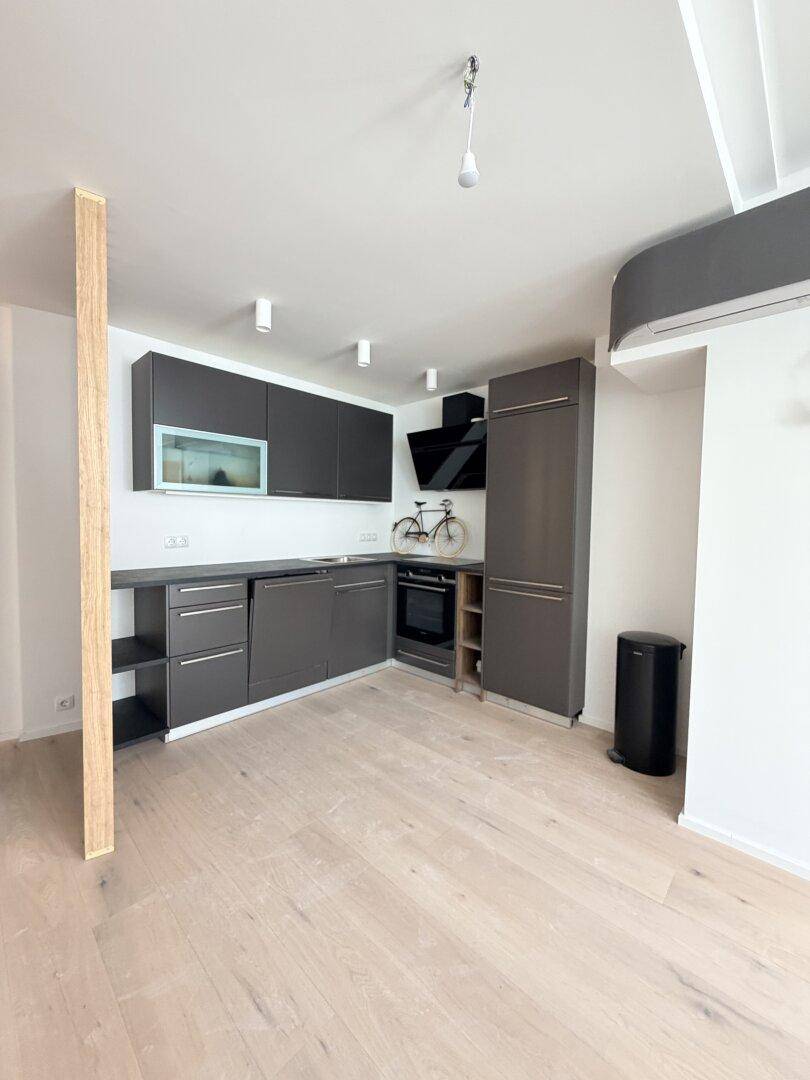 Moderne Küche mit dunkelgrauen Schränken, integriertem Backofen und Dunstabzugshaube auf hellem Holzboden.