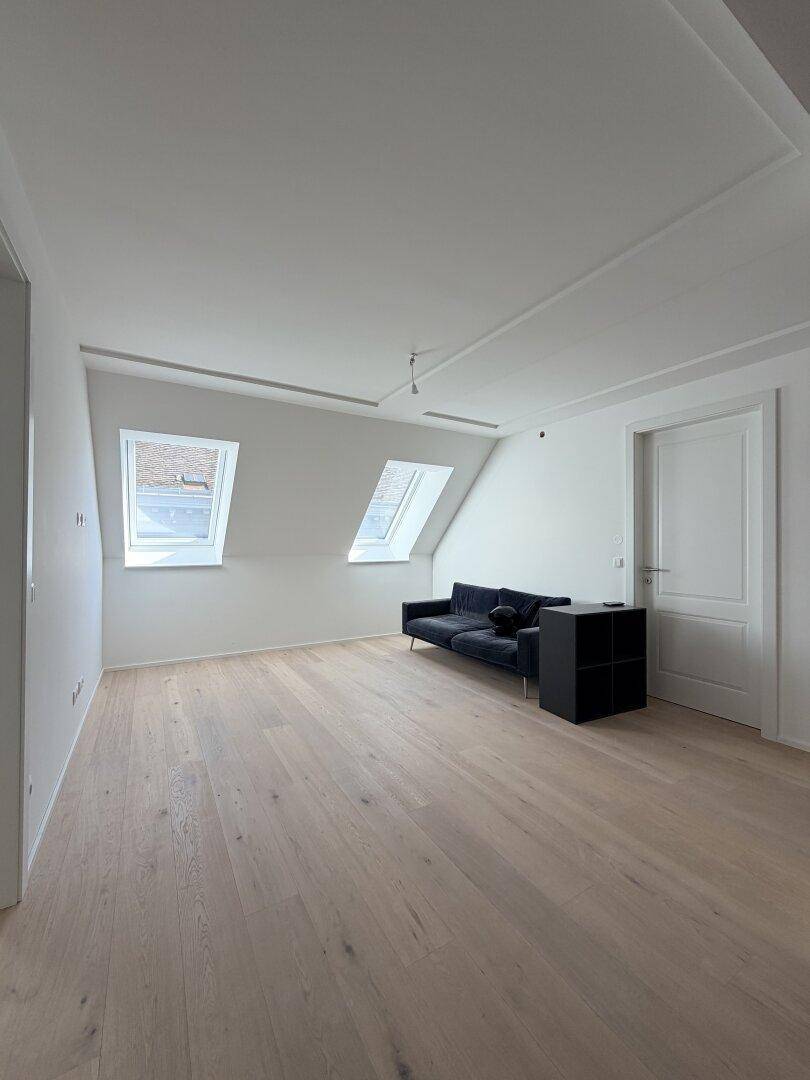 Helles Wohnzimmer im Dachgeschoss mit schrägen Wänden, zwei Dachfenstern und Holzboden.