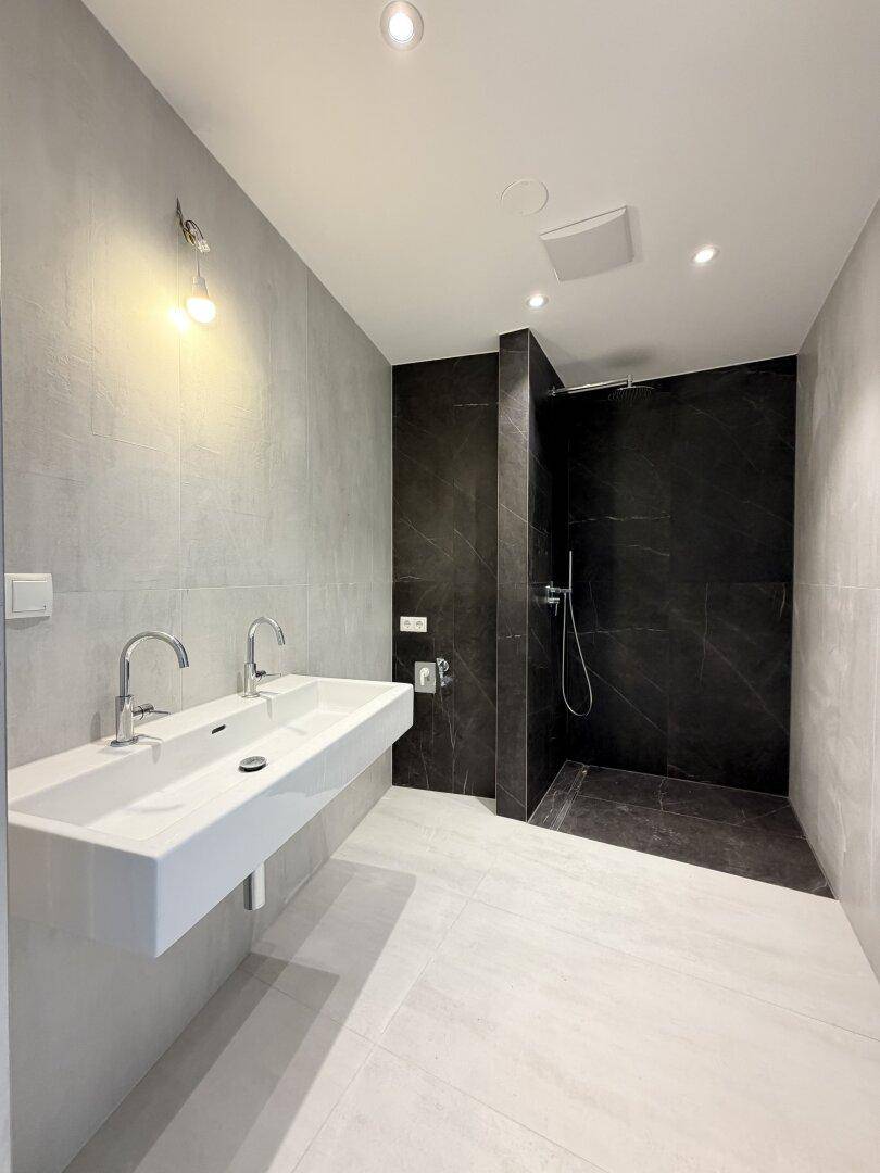 Modernes Badezimmer mit Doppelwaschbecken, großer begehbarer Dusche und grauen sowie schwarzen Fliesen.