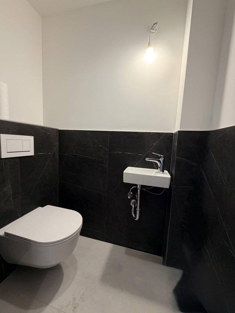 Modernes Gäste-WC mit wandhängender Toilette, kleinem Waschbecken und schwarz-weißen Fliesen.