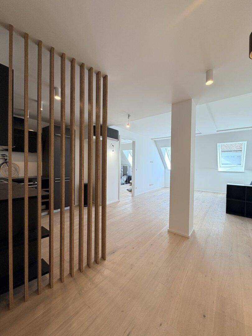Offener Wohnbereich mit Holzboden und einer dekorativen Holzlamellenwand, die zum Küchenbereich führt.