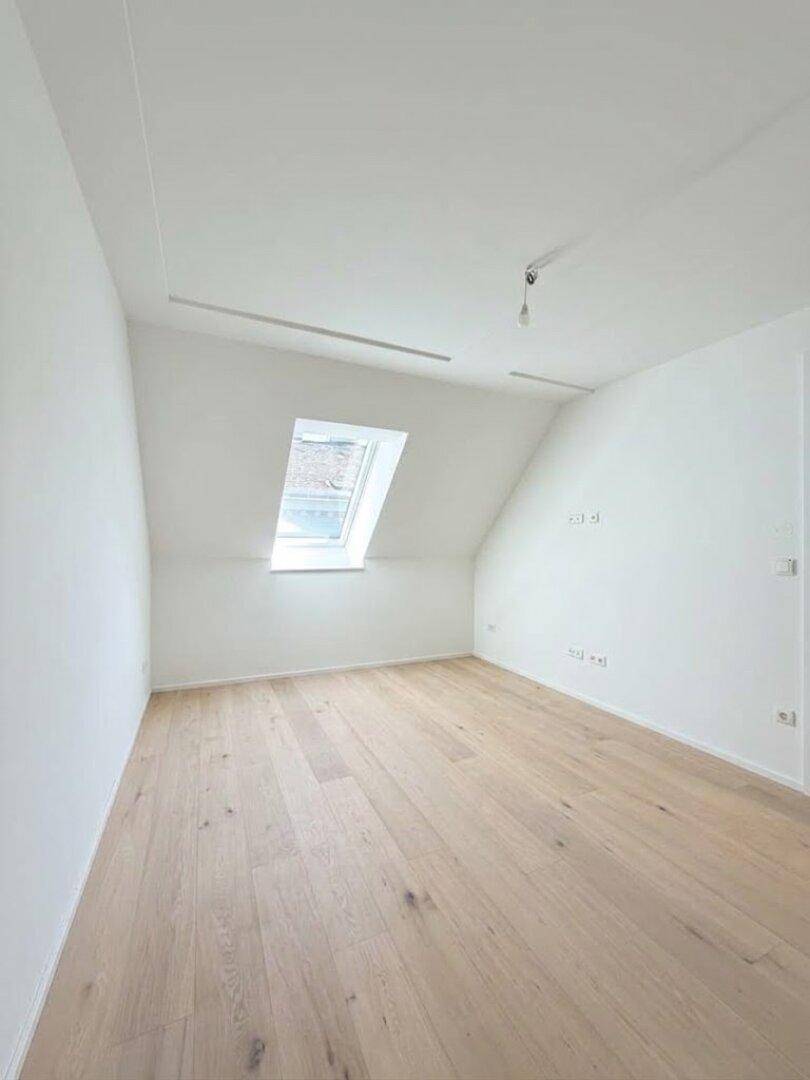Helles Schlafzimmer im Dachgeschoss mit schräger Decke, einem Dachfenster und Holzboden.