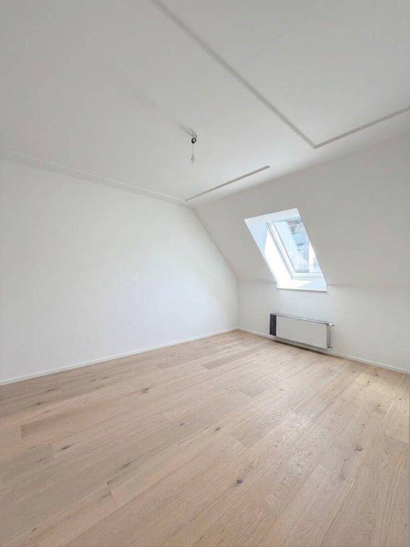 Leeres Schlafzimmer im Dachgeschoss mit schräger Decke, einem Dachfenster und hellem Holzboden.