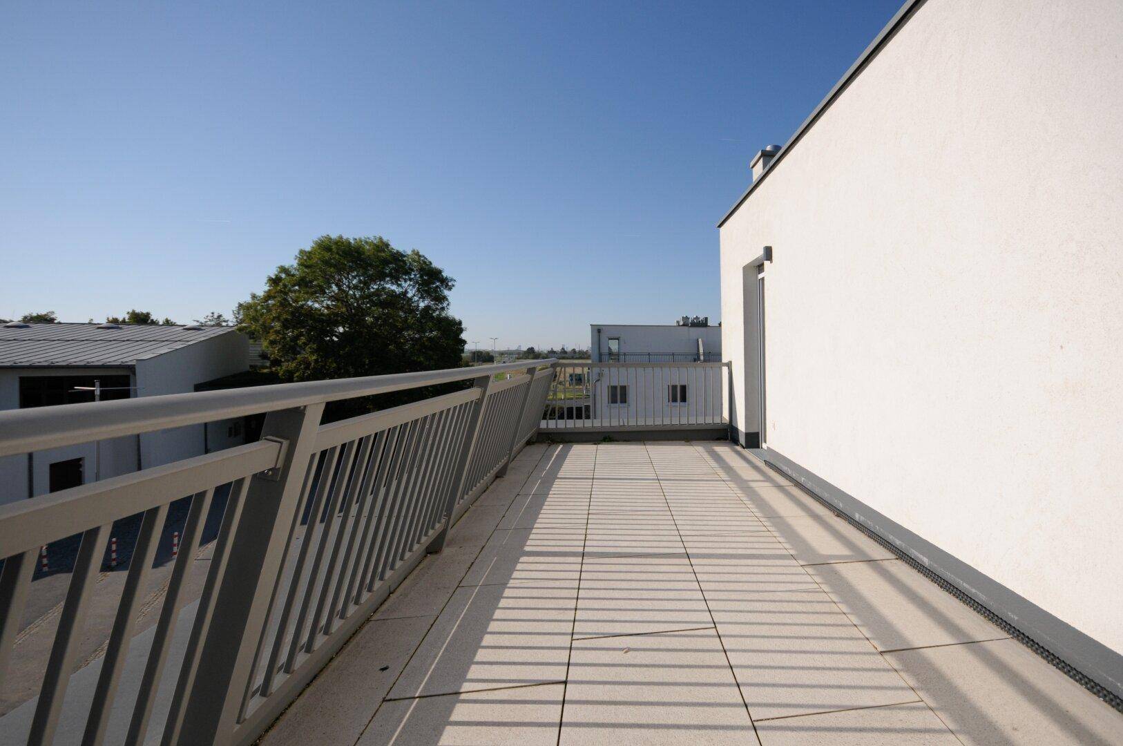 Lange Terrasse mit Fliesenboden und Metallgeländer, bietet einen weiten Blick über die Umgebung.