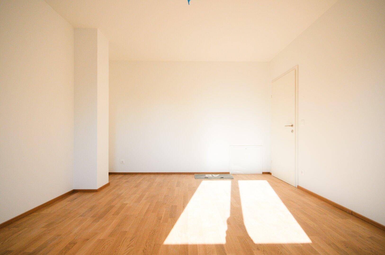 Geräumiger, heller Raum mit Parkettboden, weißen Wänden und viel natürlichem Licht.