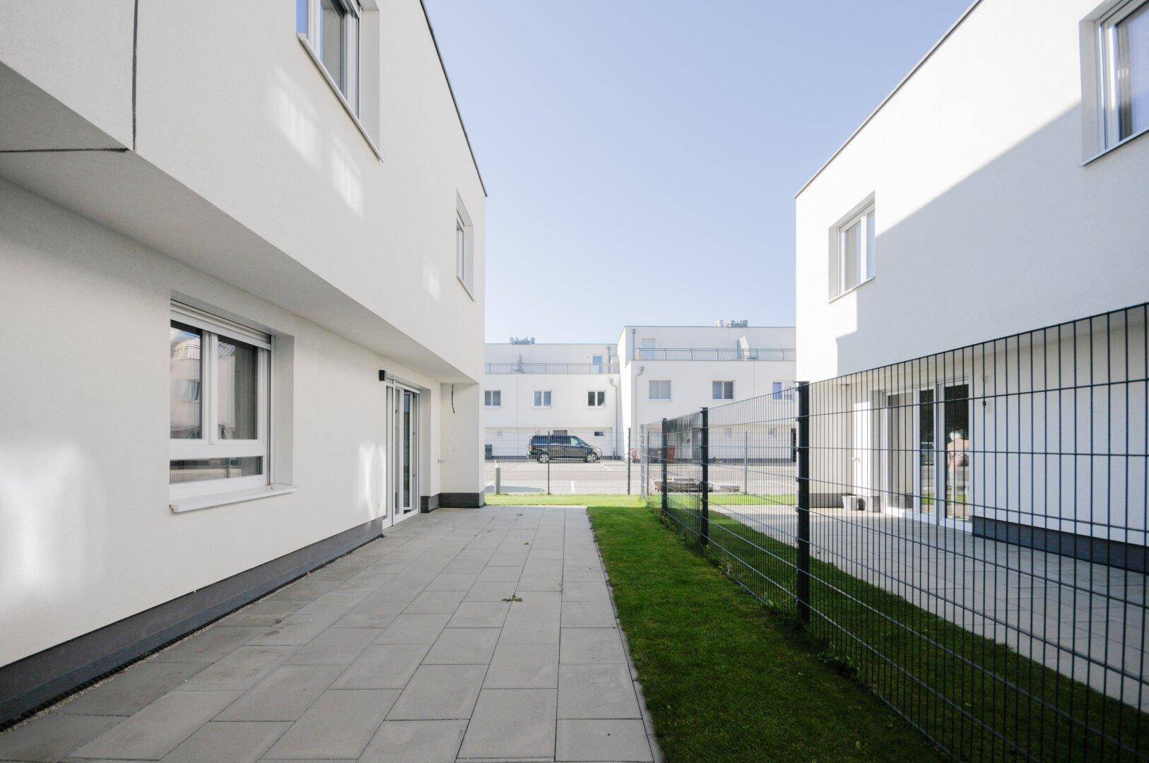 Moderne weiße Gebäude mit gepflasterten Wegen und Rasenflächen in einer Wohnsiedlung.