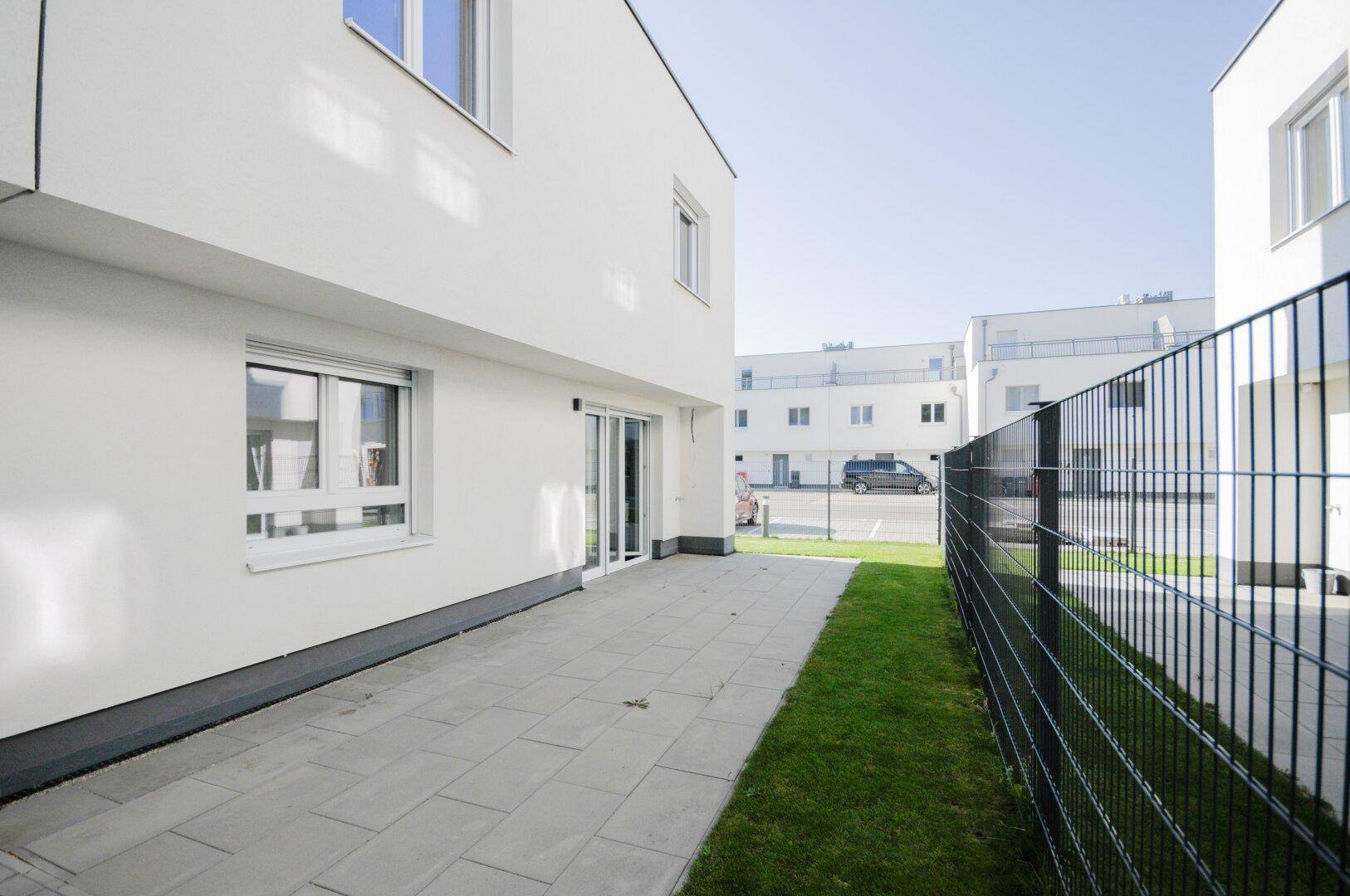 Gepflasterter Außenbereich neben dem Haus mit Rasenstreifen und Blick auf die Nachbarschaft.