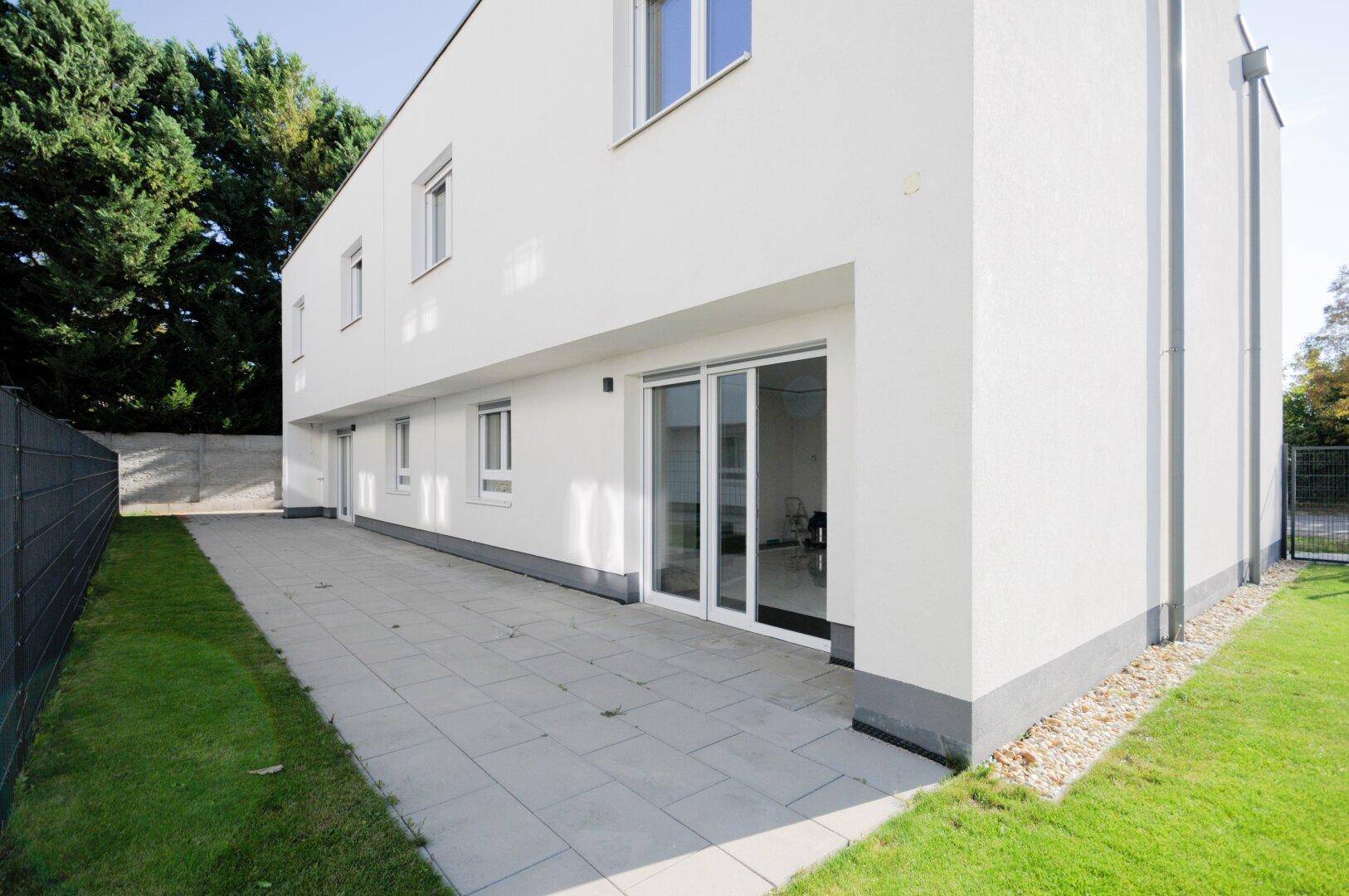 Große gepflasterte Terrasse an der Rückseite des Hauses mit Schiebetüren und Rasenfläche.