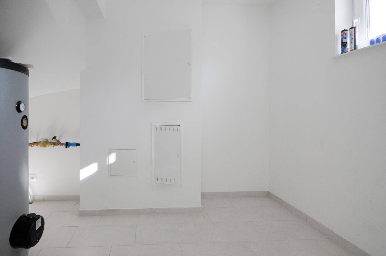 Heller Hauswirtschaftsraum mit Fliesenboden und einem Warmwasserspeicher, ideal für Technik und Lagerung.