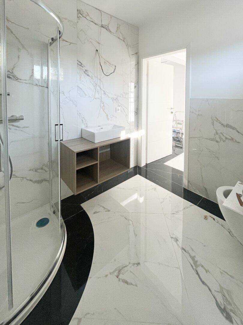 Elegantes Badezimmer mit Marmorfliesen, moderner Dusche und Waschtisch mit Stauraum.