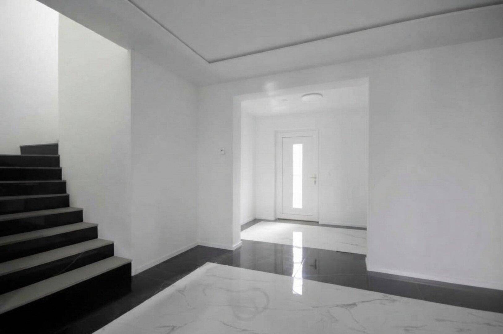 Heller Eingangsbereich mit Marmorfliesenboden, dunklem Akzent und Treppe zum Obergeschoss.