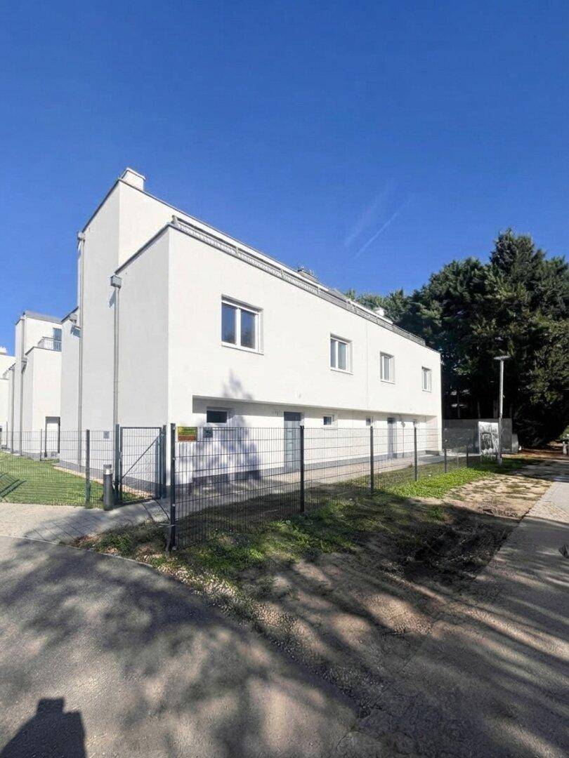 Moderne weiße Reihenhäuser mit klaren Linien und umzäunten Grünflächen unter blauem Himmel.