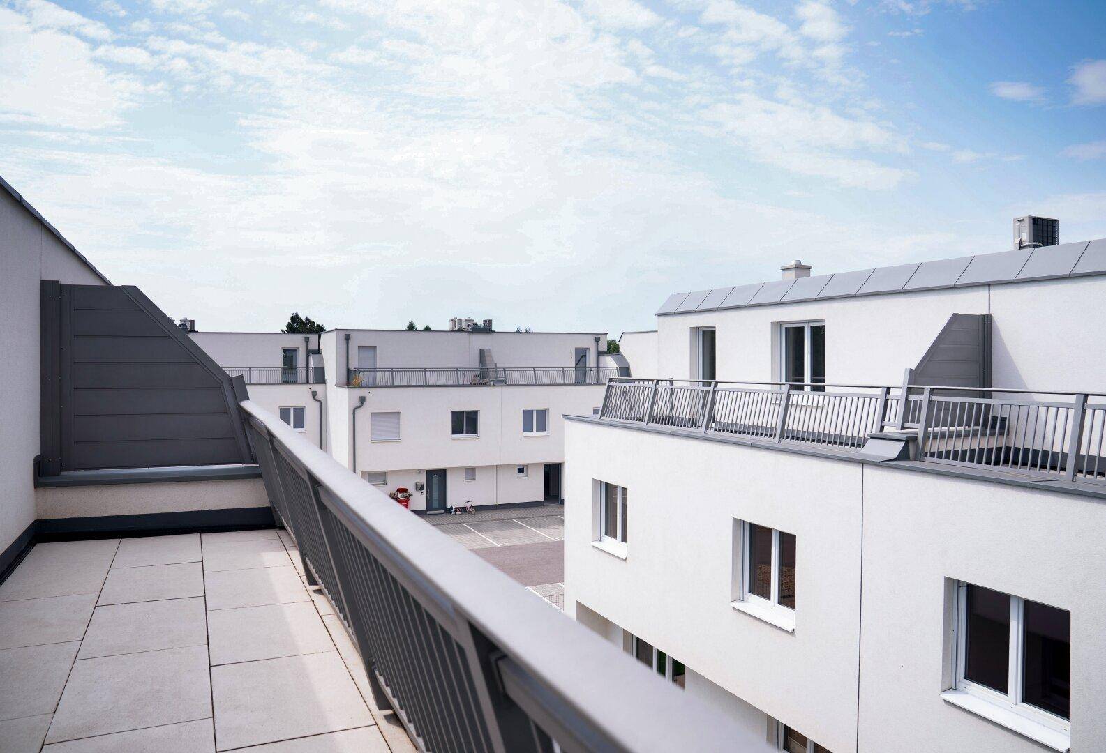 Geräumige Dachterrasse mit Fliesenboden und Blick auf weitere moderne Gebäude der Siedlung.