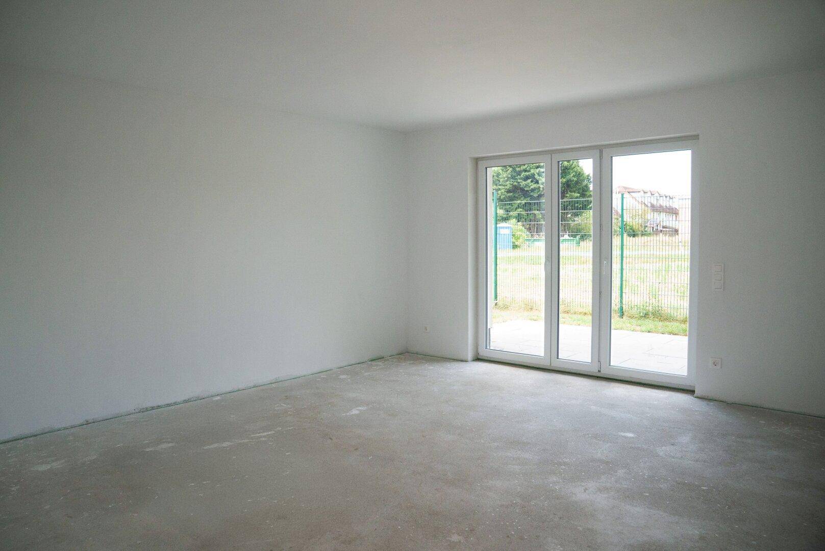 Unfertiger Wohnraum im Rohbau mit Betonboden und großen Schiebetüren zum zukünftigen Gartenbereich.