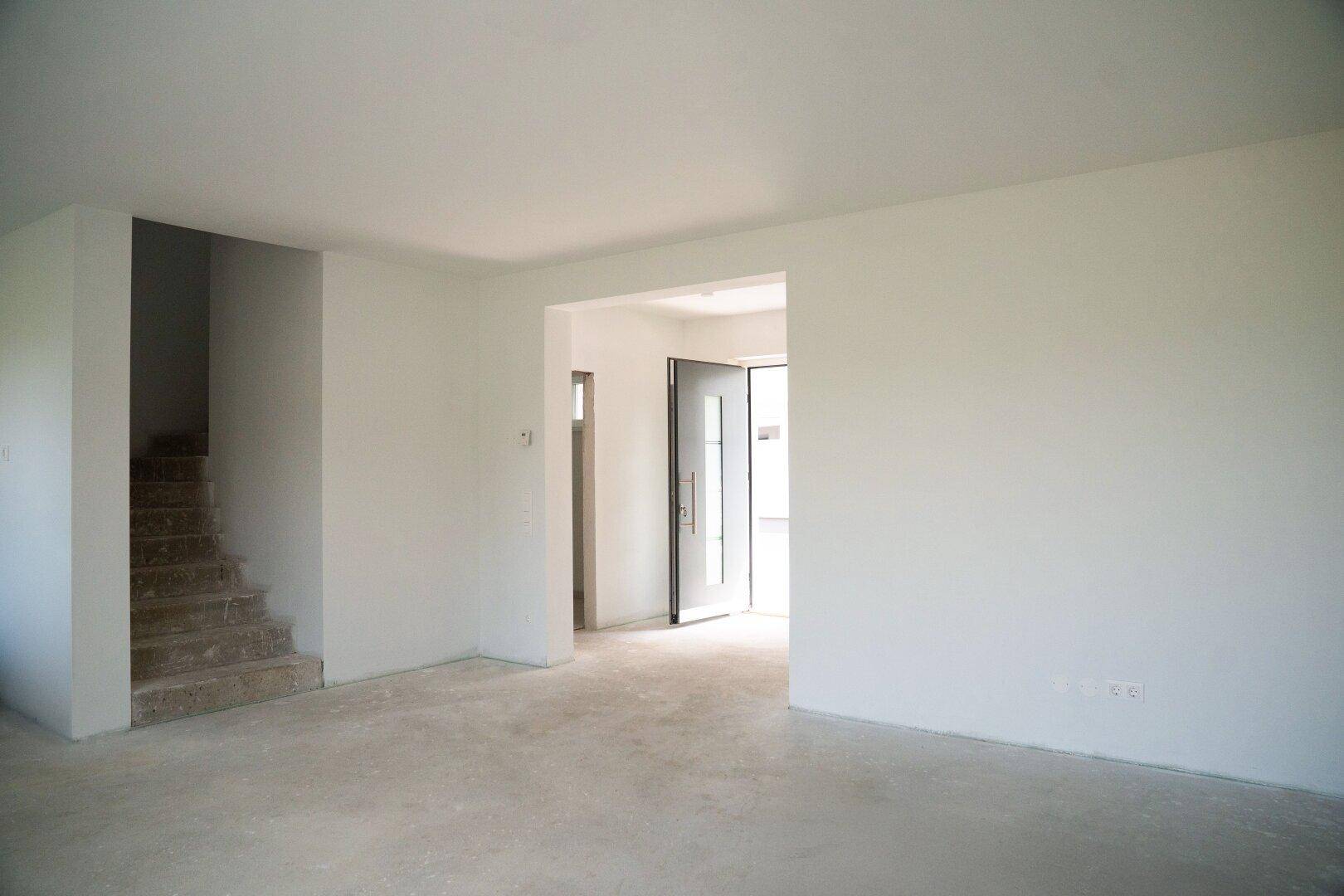 Heller Eingangsbereich im Rohbau mit Betonboden und Treppenaufgang zu den oberen Etagen des Hauses.
