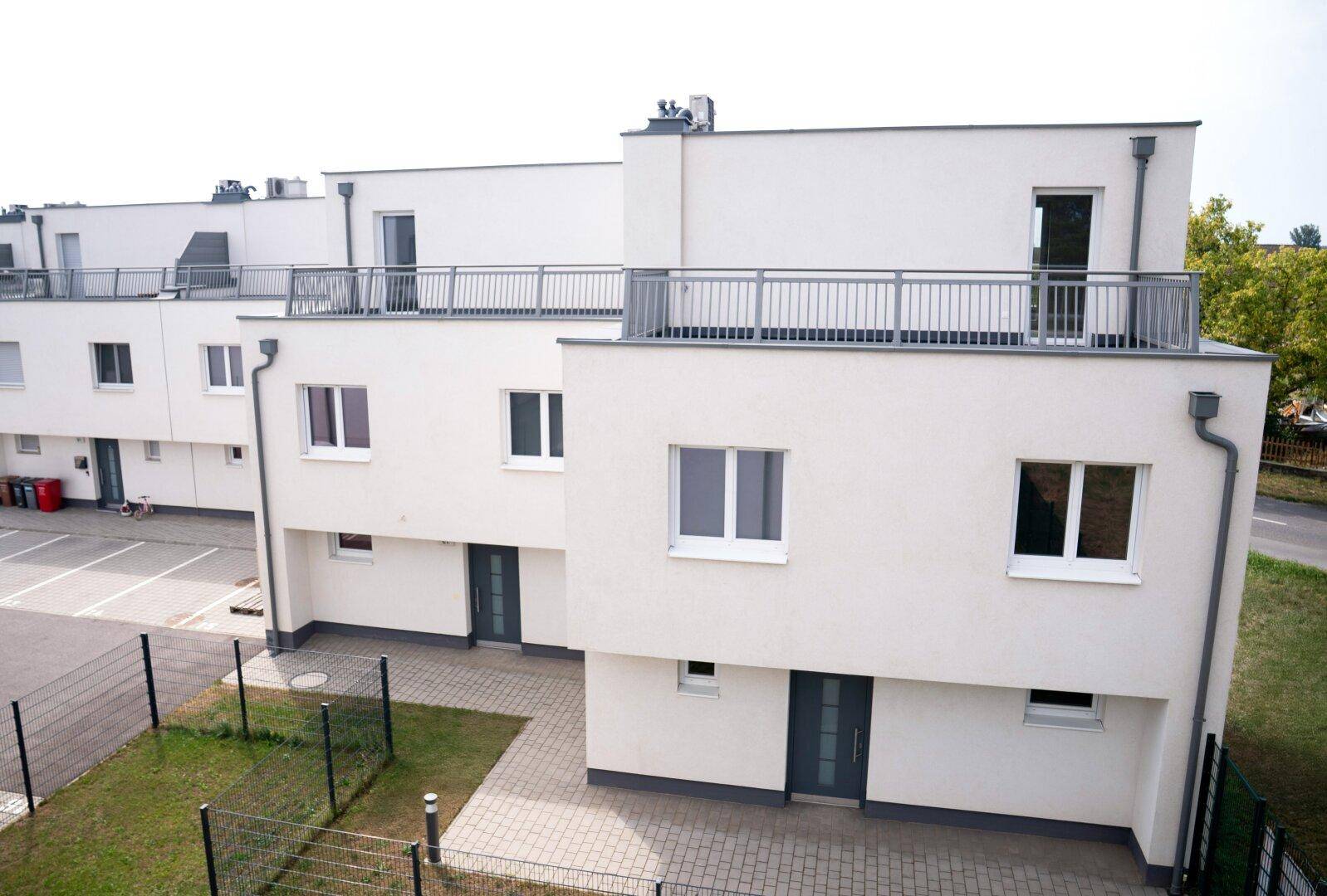 Vogelperspektive auf eine Siedlung moderner Reihenhäuser mit Gärten und Parkplätzen vor den Eingängen.