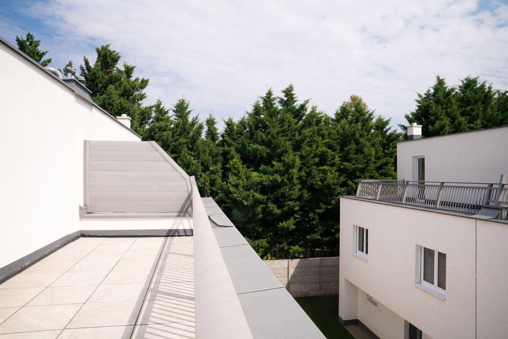 Dachterrasse mit Fliesenboden und einem ruhigen Blick auf grüne, hohe Bäume in der Umgebung.