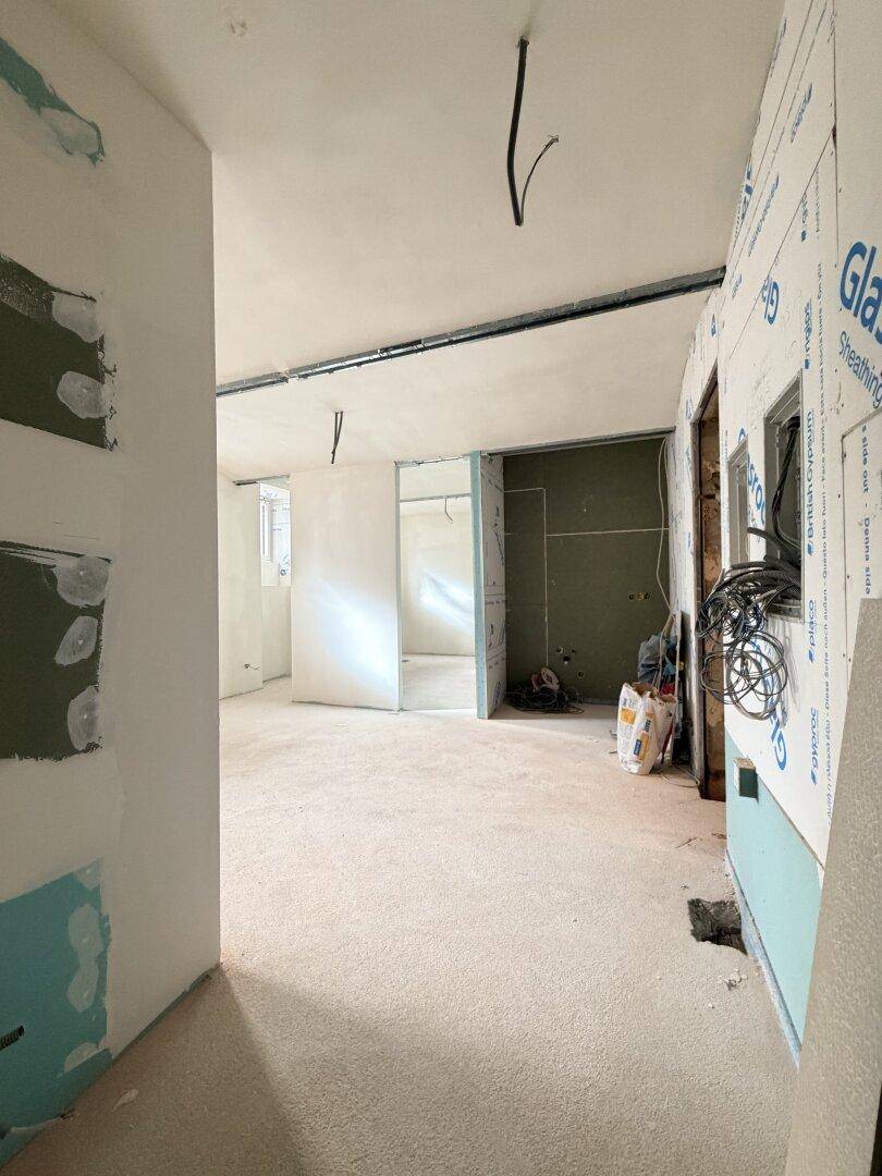 Innenraum im Rohbauzustand mit unverputzten Wänden, sichtbaren Installationen und Baustoffen.