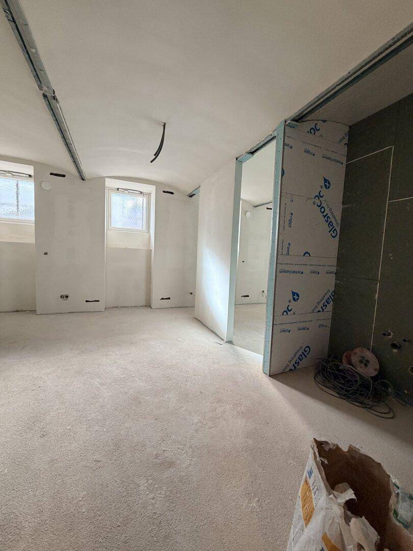 Rohbau eines Innenraums mit vorbereiteten Wänden, Fenstern und sichtbaren Bauelementen.