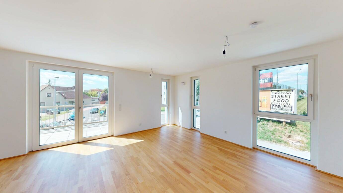 Helles Wohnzimmer mit Parkettboden und großen Fenstern mit Blick nach draußen.
