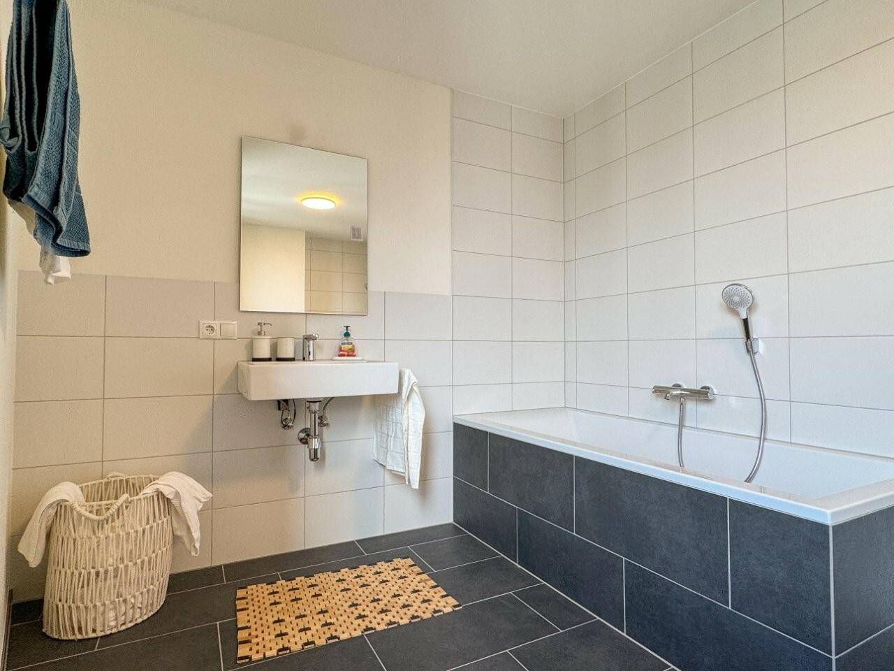Modernes Badezimmer mit Badewanne, Waschbecken und stilvollen Fliesen in Weiß und Anthrazit.