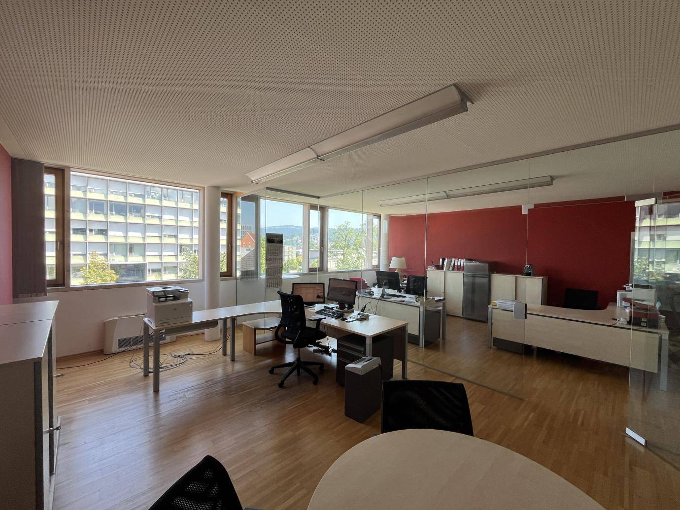 Weitläufiges Büro mit großen Fenstern, die einen Blick auf die Stadt bieten, und Holzboden.