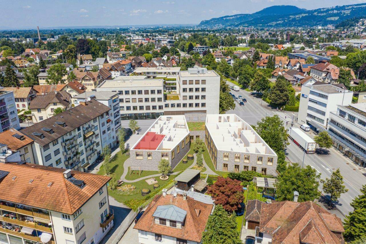 Luftaufnahme einer Wohngegend mit modernen Neubauten, umgeben von viel Grün und mit Bergblick.