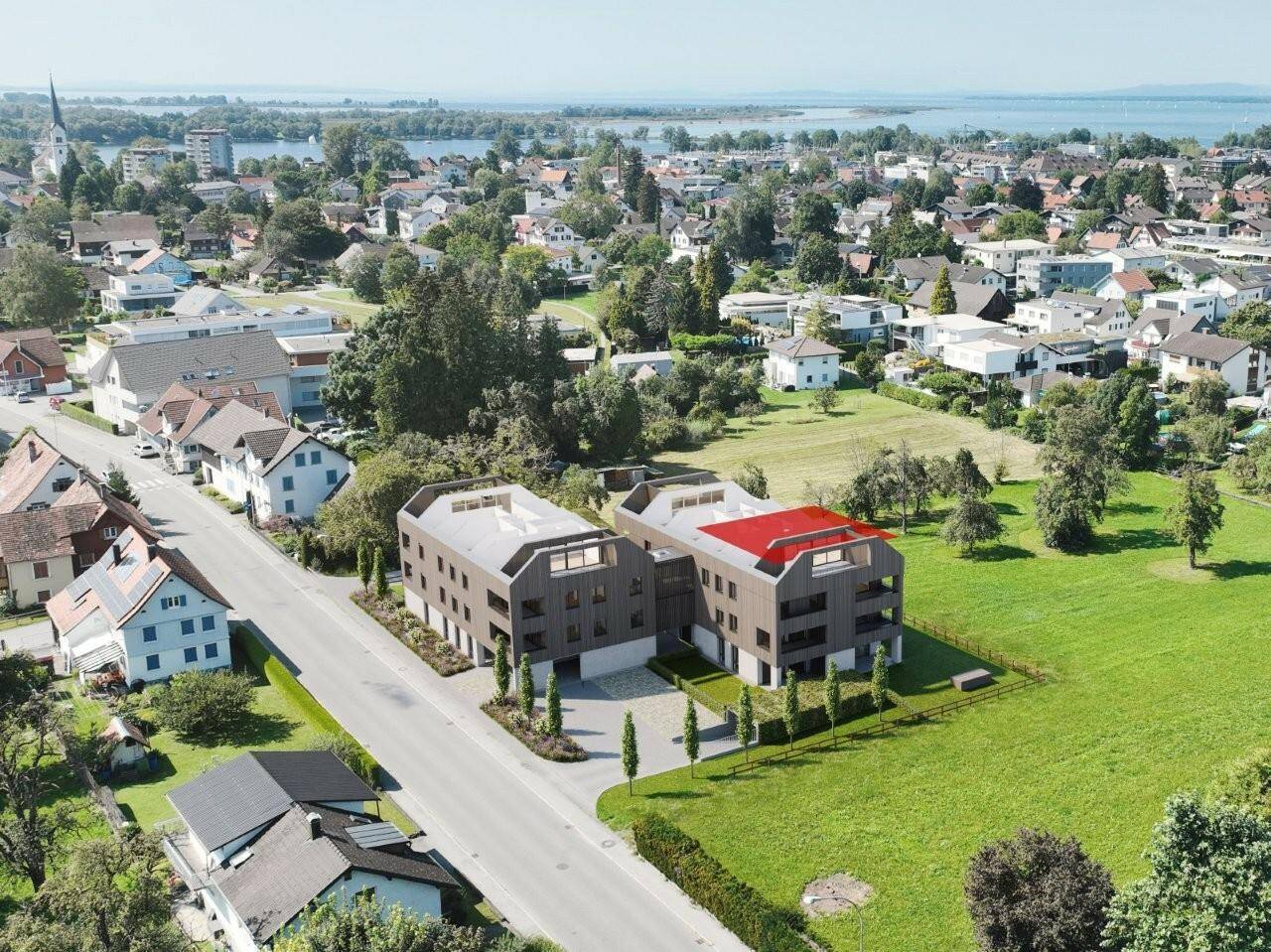 Eine Luftaufnahme von zwei modernen Mehrfamilienhäusern mit Satteldach in einer ländlichen Umgebung nahe dem Bodensee. Eines der Dächer ist rot markiert (Konfigurator).