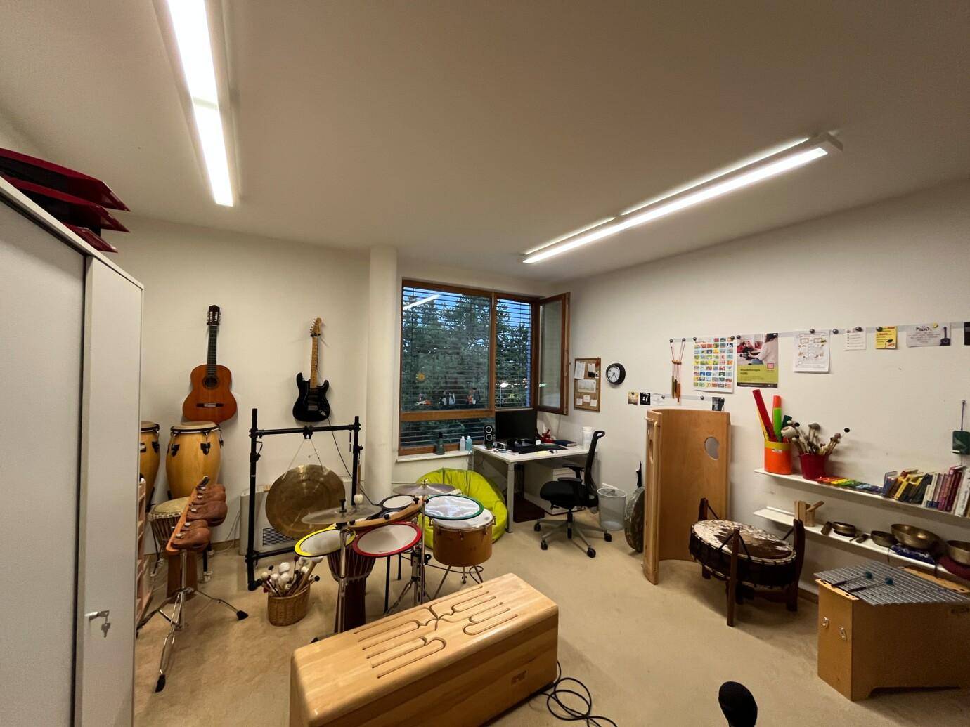 Musik- oder Therapieraum mit verschiedenen Instrumenten, Schreibtisch und einem Fenster mit Blick ins Grüne.