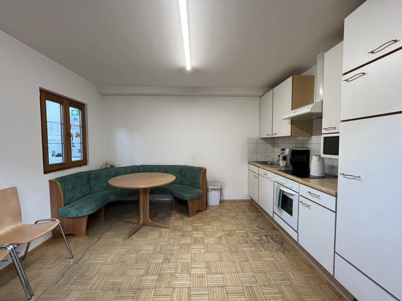 Kleine Küche oder Pausenraum mit weißen Schränken, Einbauherd, Spüle und einer gemütlichen Eckbank mit Tisch.