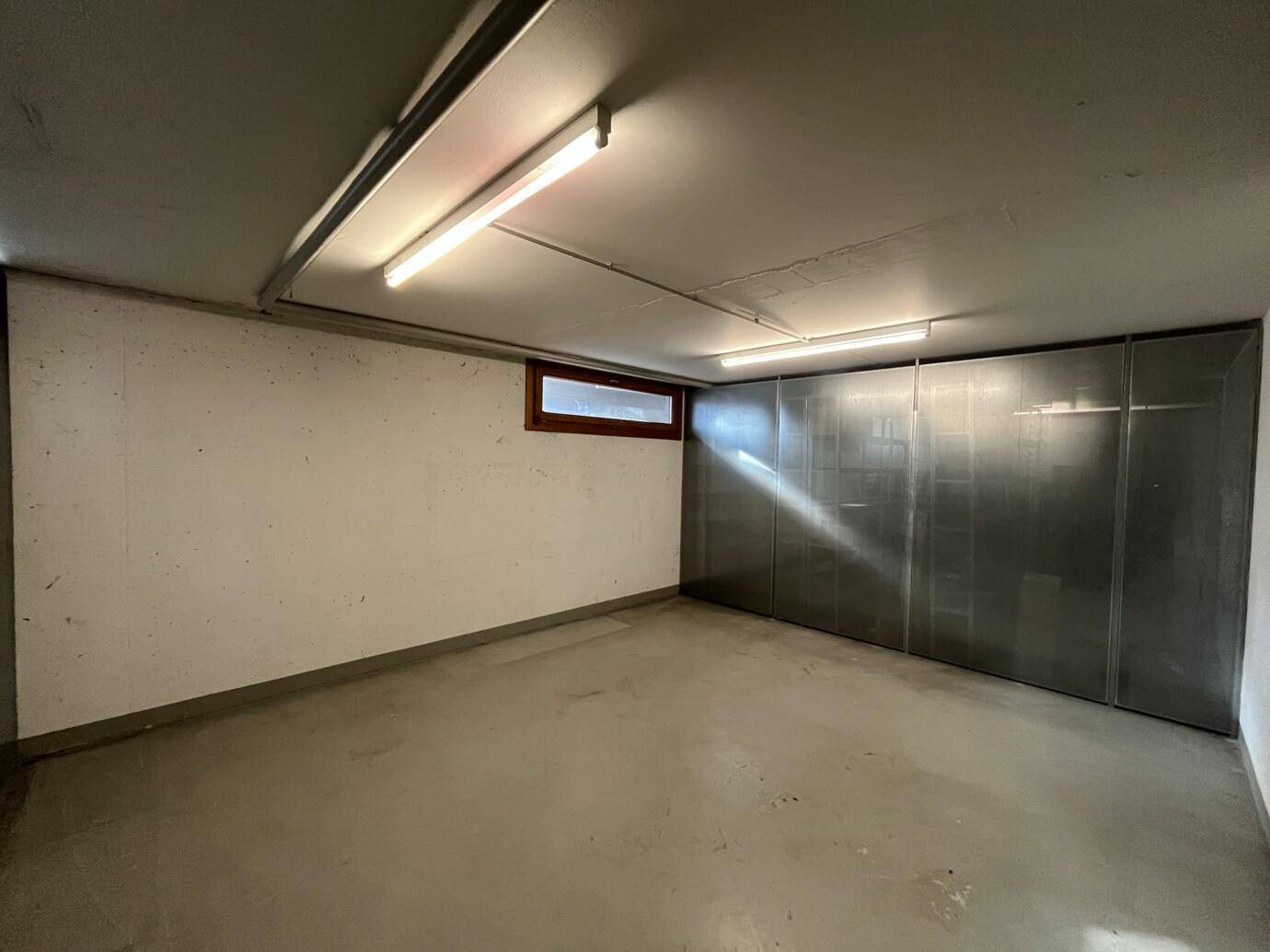 Geräumiger Lagerraum im Keller mit Metallabtrennungen und kleinem Fenster.