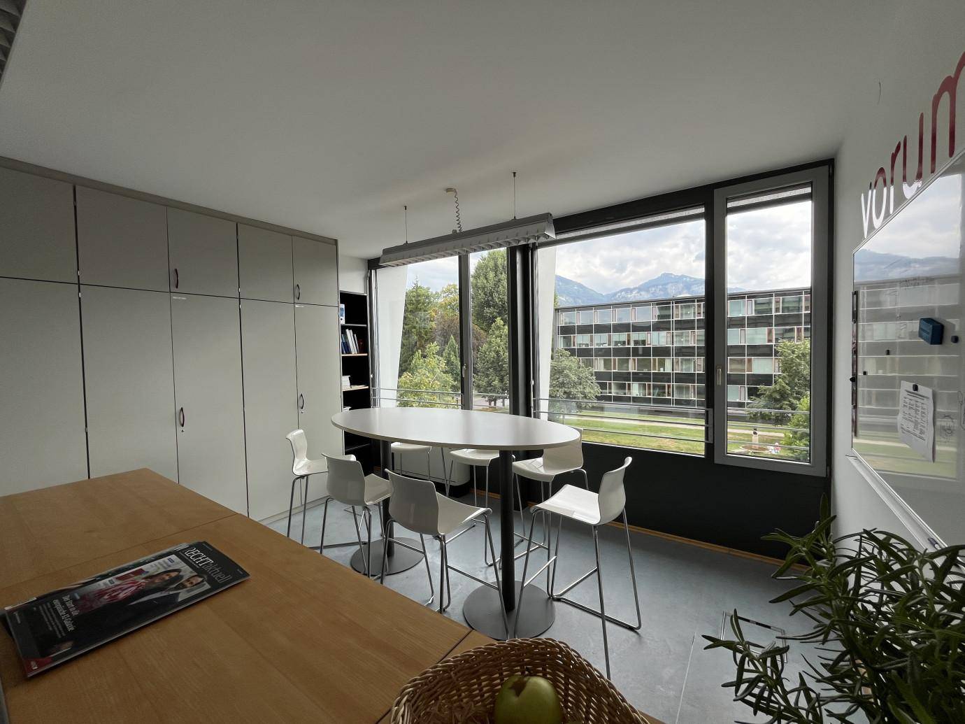 Informeller Besprechungsbereich mit Stehtisch, Barhockern und grüner Aussicht durch die Fenster.
