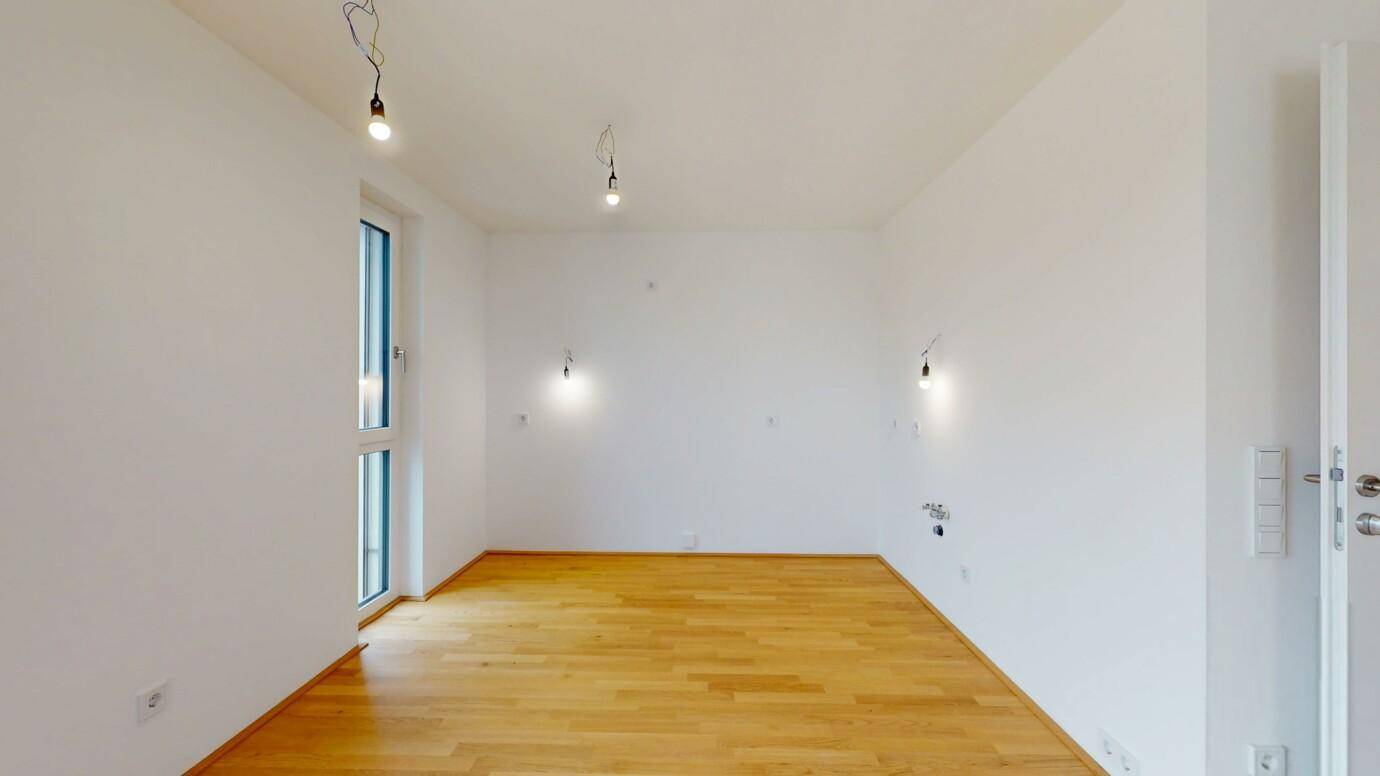 Leeres Schlafzimmer mit hellem Holzparkett und einem hohen Fenster für viel Tageslicht.