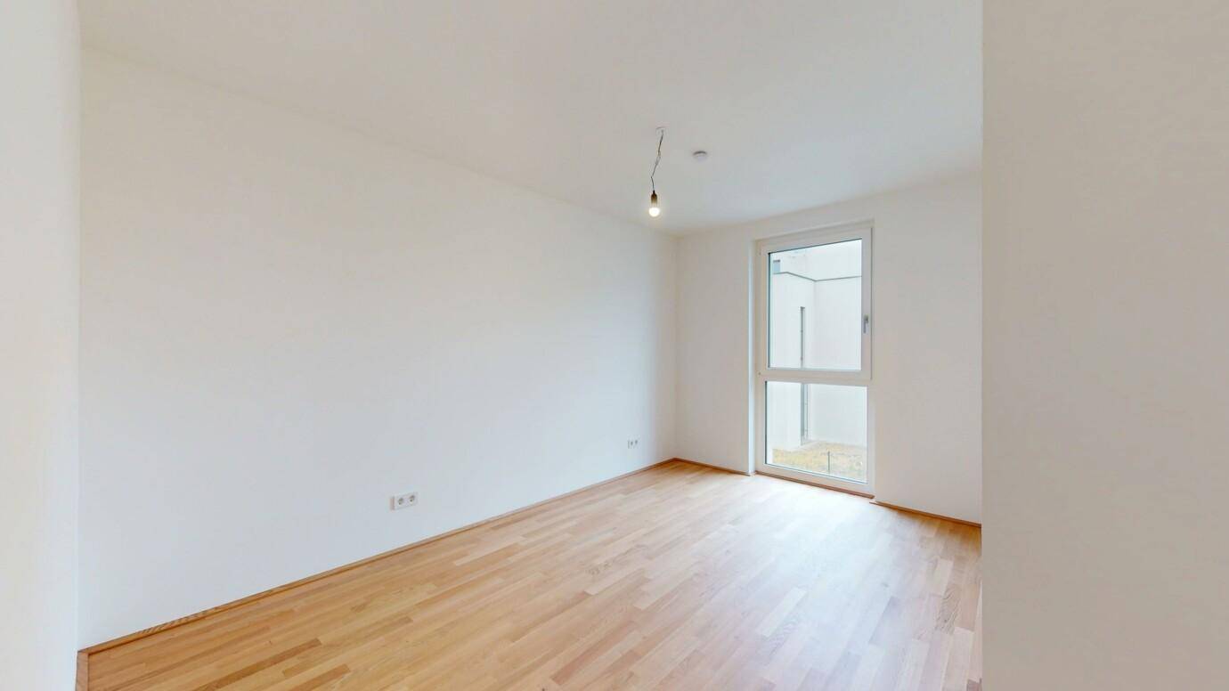 Helles Zimmer mit Holzboden und großem Fenster, ideal als Schlaf- oder Arbeitszimmer.