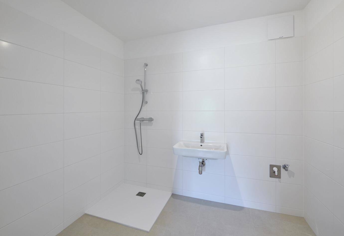 Modernes Badezimmer mit weißen Fliesen, ebenerdiger Dusche und einem einzelnen Waschbecken.