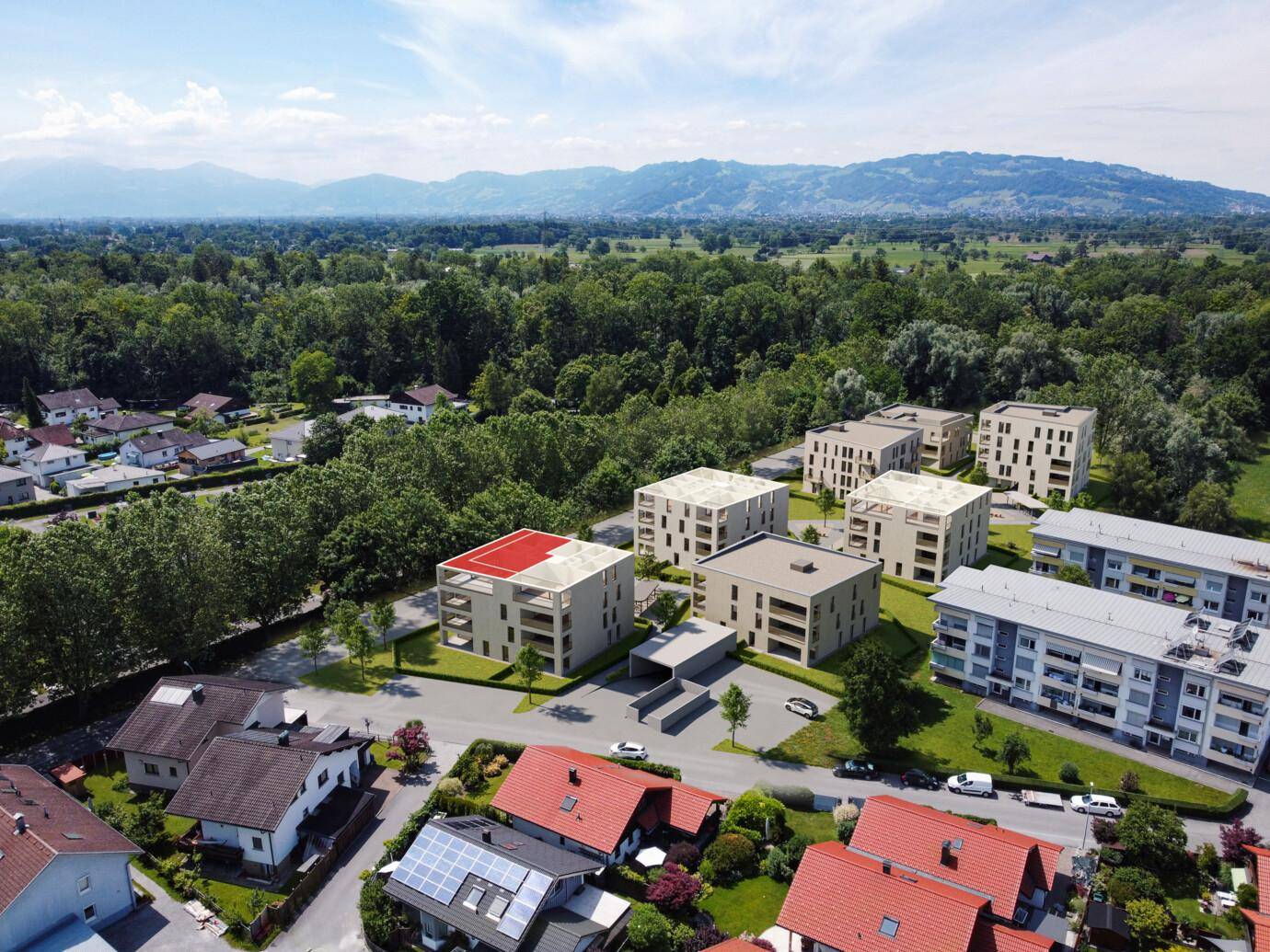 Luftaufnahme einer modernen Wohnanlage mit mehreren Gebäuden, umgeben von Natur und Bergblick.