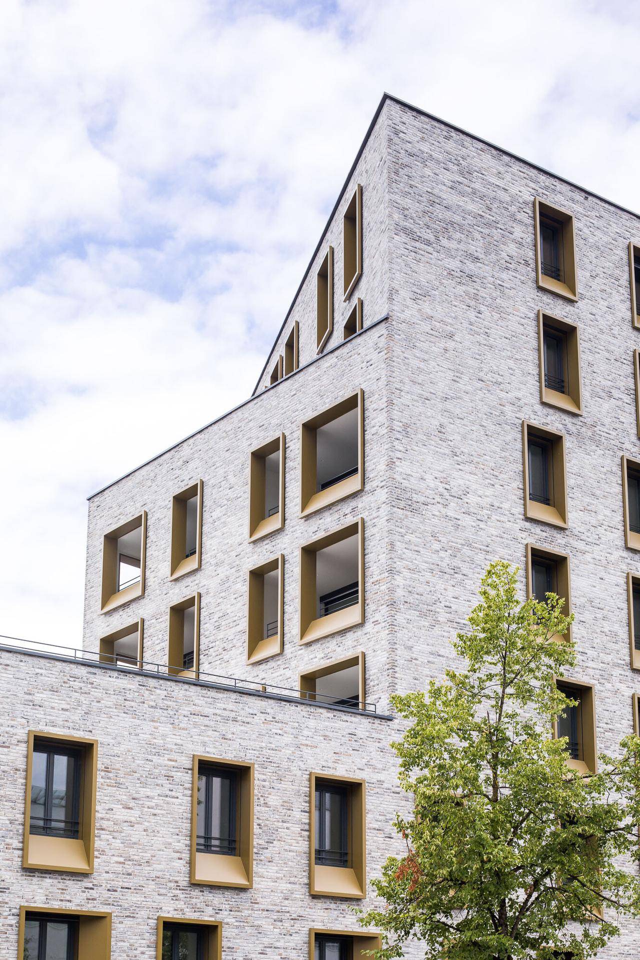 Detailansicht der modernen Gebäudefassade mit hellen Ziegeln und goldenen Fensterrahmen.