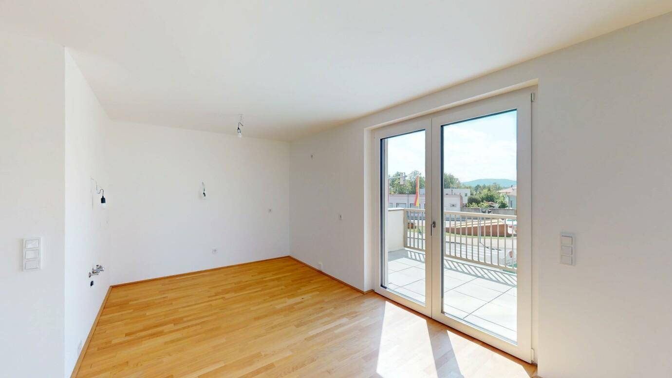 Heller Wohnbereich mit Zugang zu einem Balkon und Blick auf die Umgebung.