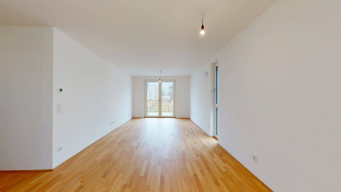 Langes, helles Wohnzimmer mit Holzboden und Zugang zu einem Außenbereich.