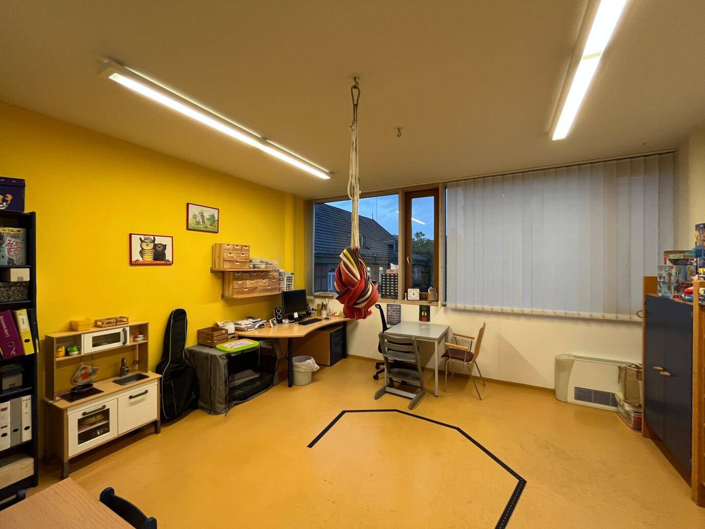 Heller Raum mit gelber Wand, Schreibtisch, Kindermöbeln und einem Schaukelhaken an der Decke.