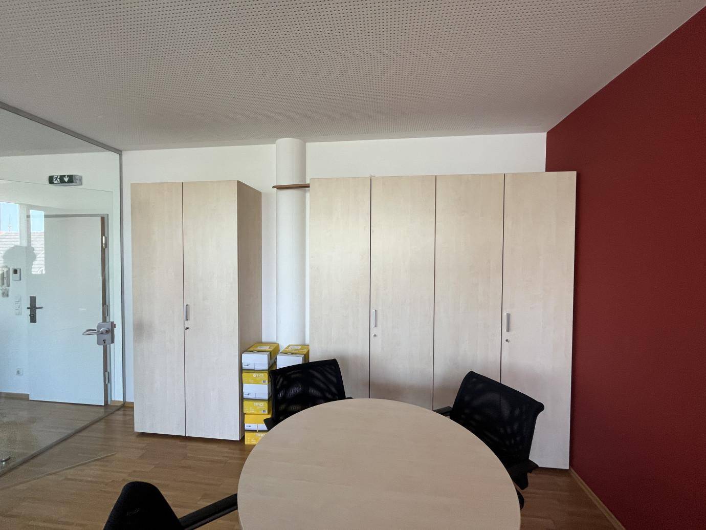 Bürobereich mit hellen Einbauschränken, einem runden Tisch und Holzboden.