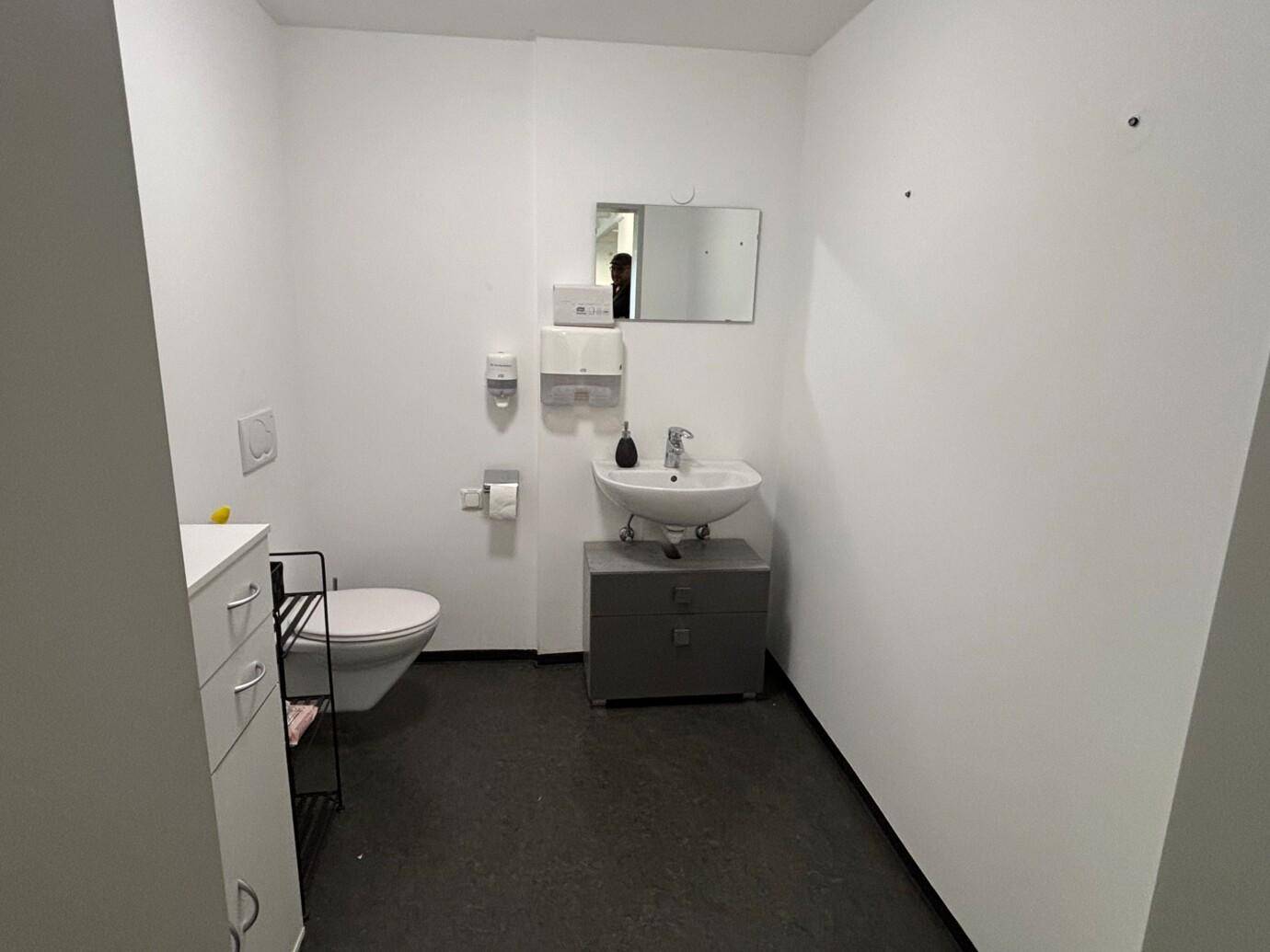 Funktionales Badezimmer mit WC, Waschbecken und Spiegel, in schlichtem Design.