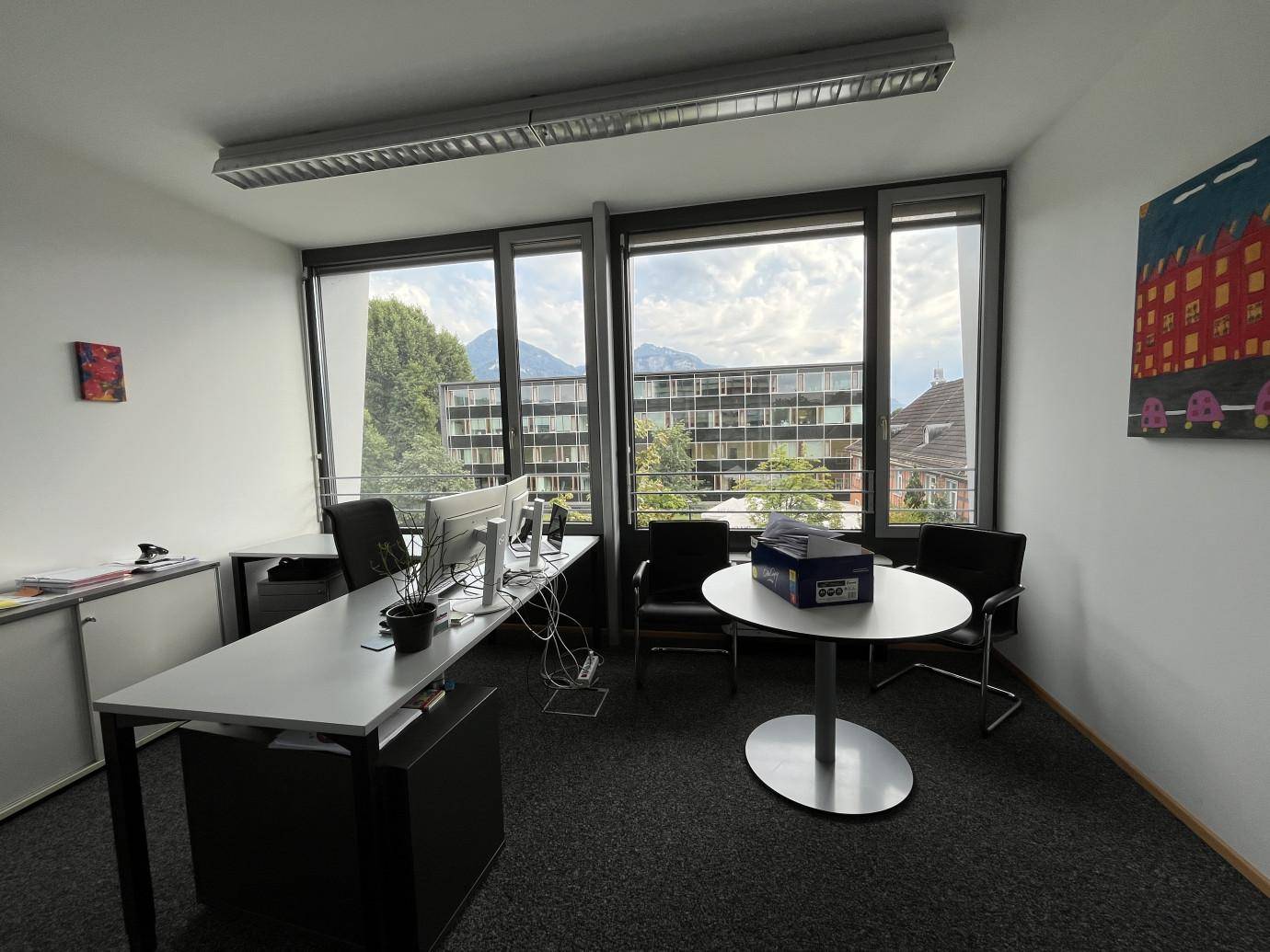 Helles Büro mit Schreibtisch, Besprechungstisch und weitem Blick auf die Umgebung und Berge.