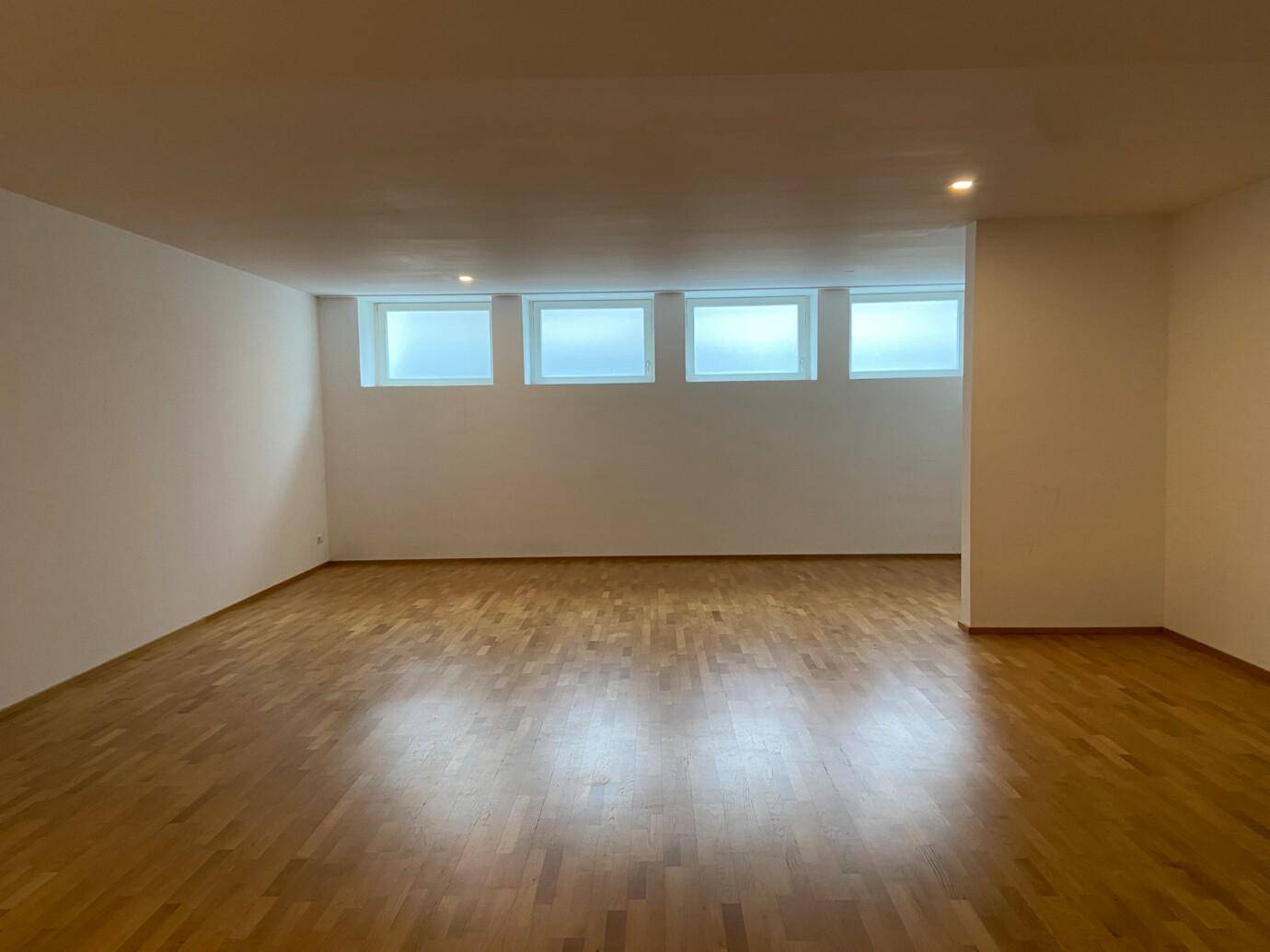 Heller, leerer Raum mit Holzboden und hohen Fenstern, ideal für vielfältige Nutzung.