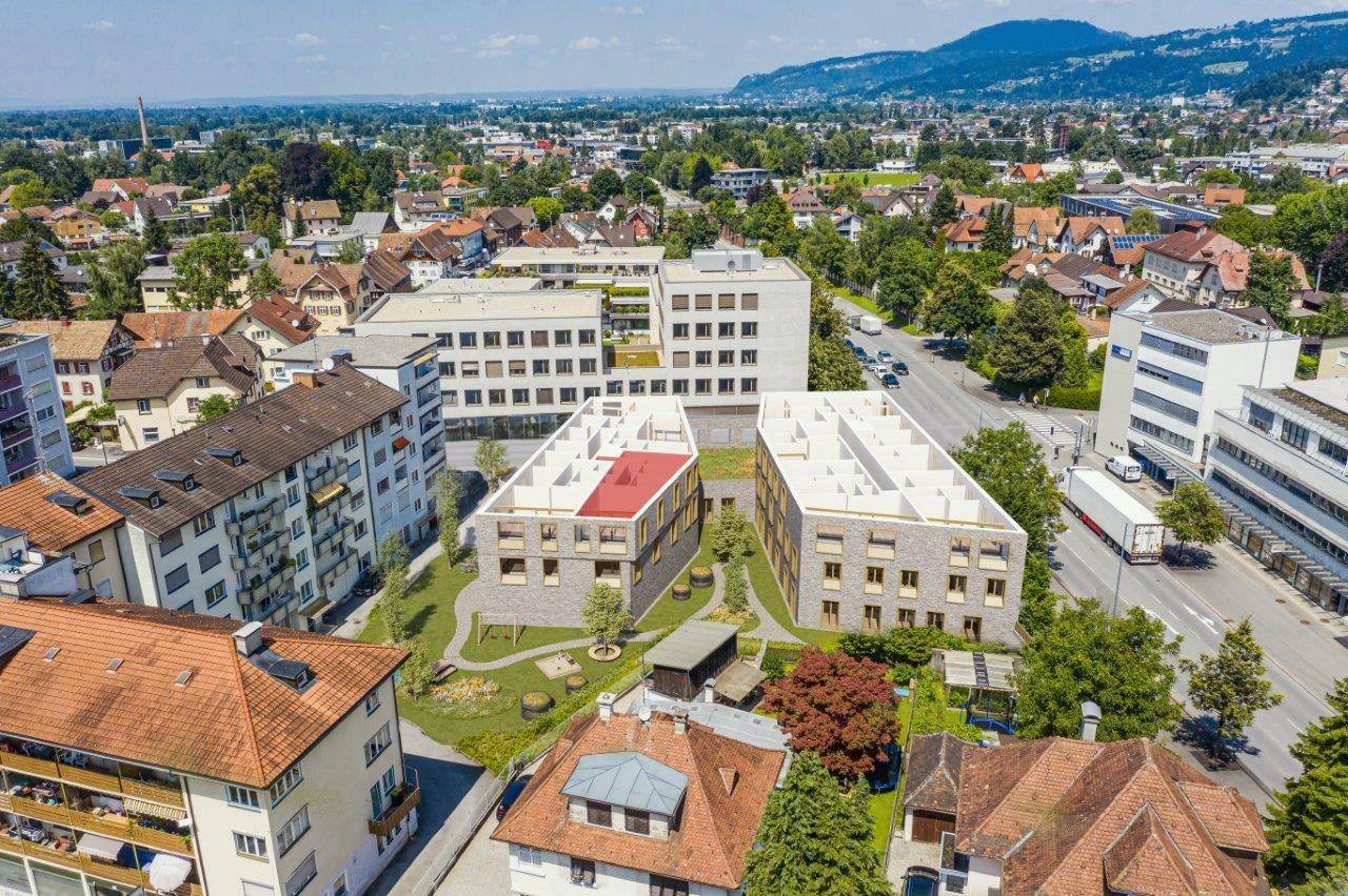 Luftaufnahme von modernen Neubauten in einer Wohngegend mit viel Grün und Bergen im Hintergrund.