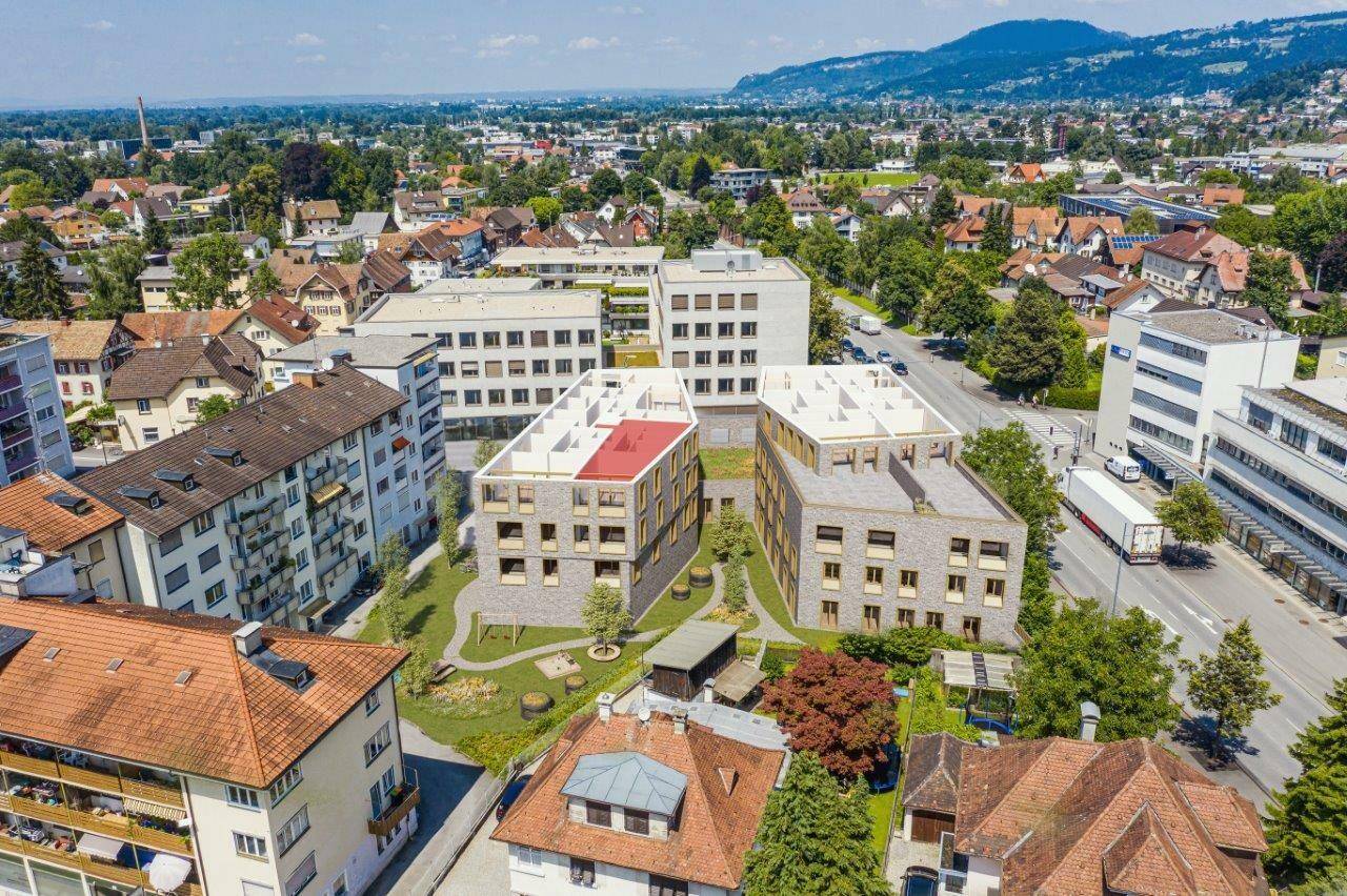 Luftaufnahme eines Neubauprojekts in einer städtischen Umgebung mit viel Grün und Bergblick im Hintergrund.