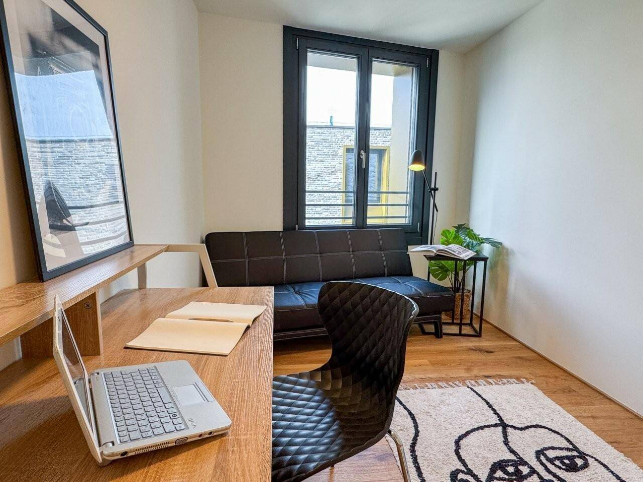 Helles Arbeitszimmer mit Holzboden, Schreibtisch und Fenster zum Innenhof.