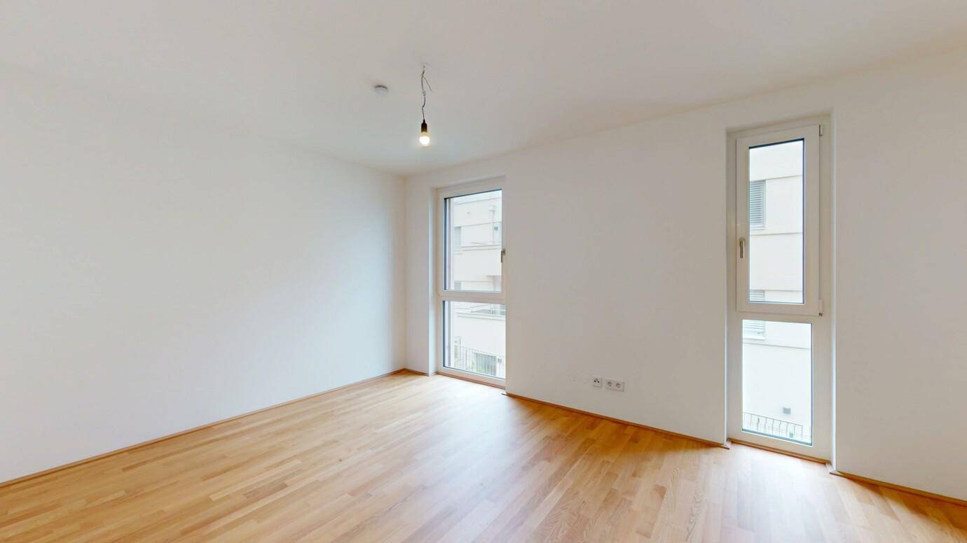 Helles, unmöbliertes Zimmer mit Holzparkett und zwei Fenstern für natürliche Belichtung.