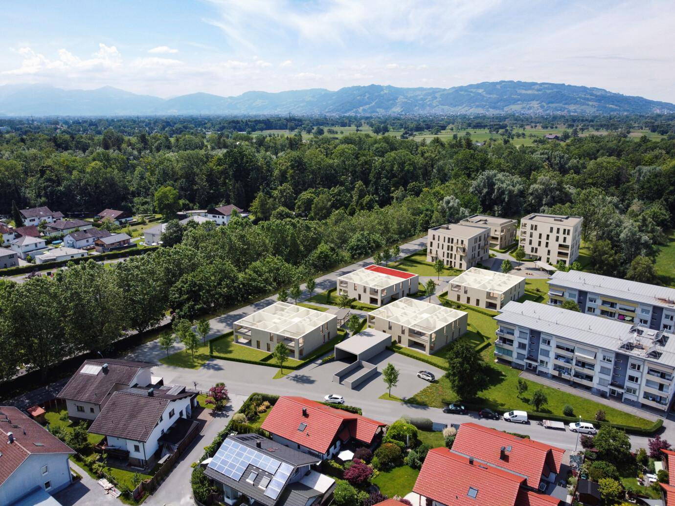 Luftaufnahme eines modernen Wohnkomplexes in einer grünen, ländlichen Umgebung mit Bergen im Hintergrund.