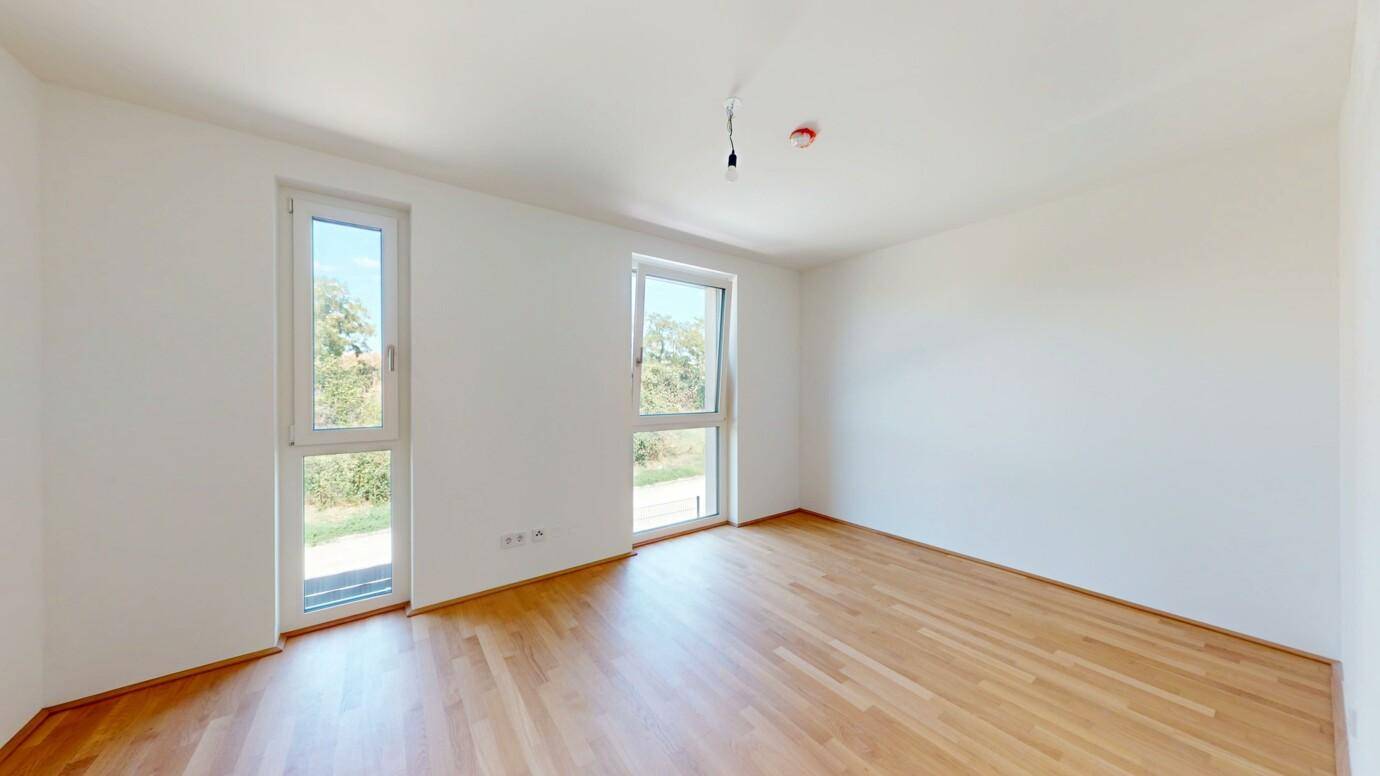 Geräumiges Zimmer mit zwei Fenstern, Holzboden und viel natürlichem Licht.